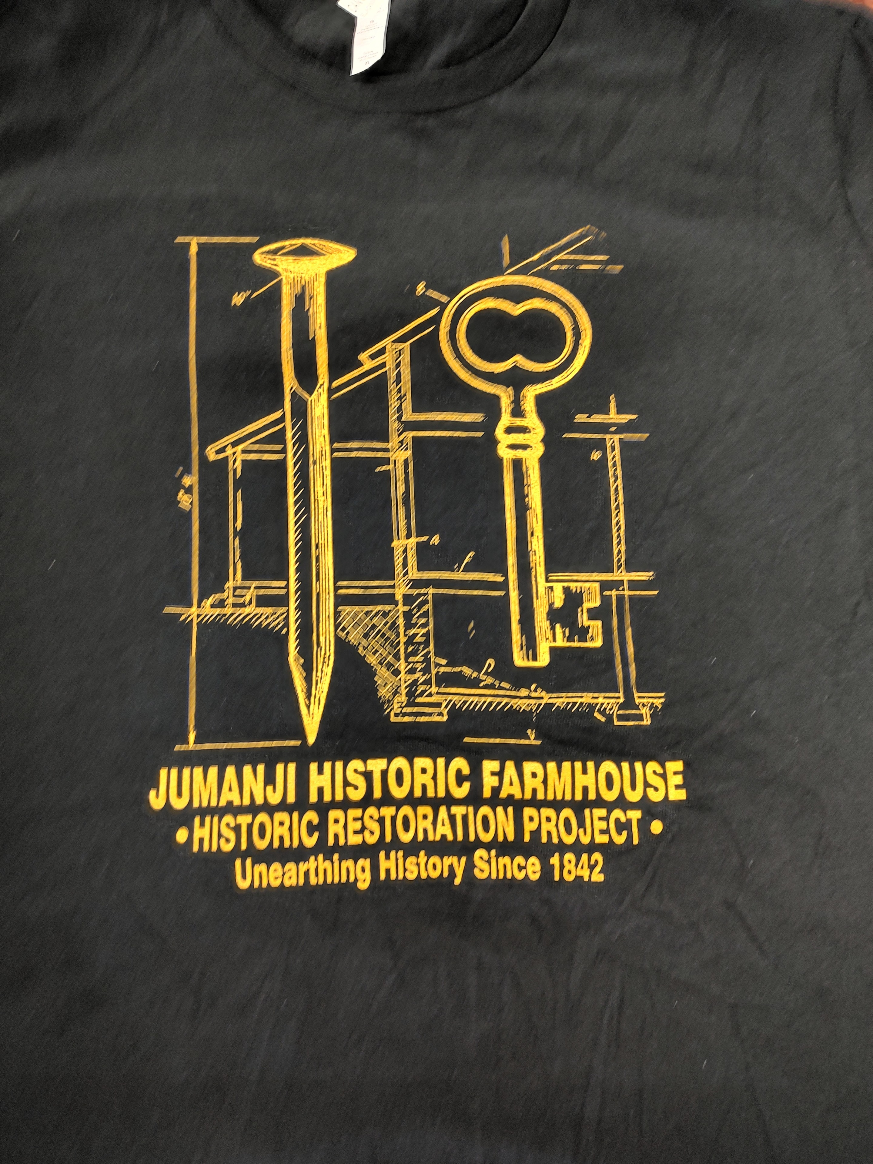 Front of a black Jumanji Historic Farmhouse Historic Restoration Project T-shirt with gold artwork